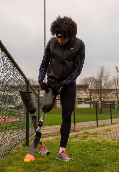 Pierna prostética con un diseño de fibra de carbono negra, unida a un conector metálico, contra un campo de hierba, con un pie colorido.