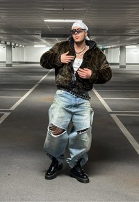 Ψεύτικο γούνα καφέ μπουφάν, λευκή αμάνικη μπλούζα, υπερμεγέθεις ανοιχτό μπλε τζιν με σχισίματα, μαύρες πλατφόρμες, ασημένιες αλυσίδες, γυαλιά ηλίου και μαντίλι.