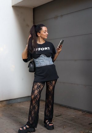 Camiseta negra oversized con el texto "EFFORT", corsé de denim, pantalones de encaje y sandalias gruesas de plataforma. Los accesorios incluyen un pequeño bolso negro.