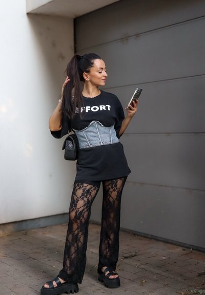 Camiseta negra oversized con el texto "EFFORT", corsé de denim, pantalones de encaje y sandalias gruesas de plataforma. Los accesorios incluyen un pequeño bolso negro.