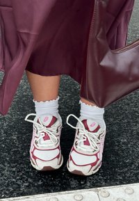 Białe i bordowe buty biegowe wykonane z siateczki i gumy, z okrągłymi sznurówkami i różowym akcentem. Noszone z białymi skarpetkami z falbankami do kostek.