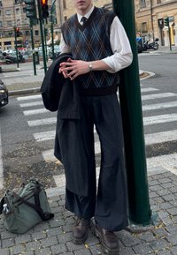 Adīta argaila veste brūnā, zilā un baltā krāsā pār baltu kreklu, kopā ar svītrainām plaša piegriezuma biksēm un tumši brūnām zābakām. Pār pleciem pārmests tumšs mētelis.