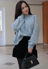 Pull gris en maille à coupe ample, associé à une jupe noire en velours à volants. Porte un sac à main noir structuré avec des ferrures dorées.