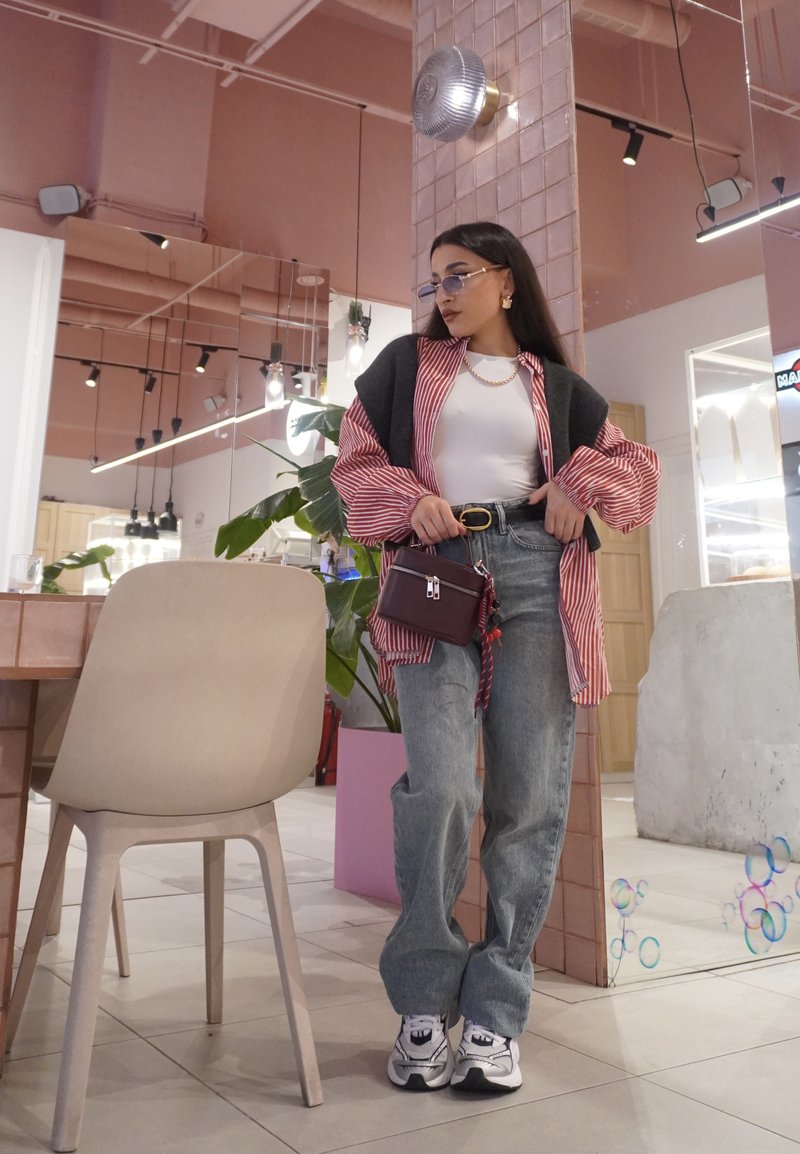 Gestreiftes rotes und weisses Oversize-Hemd über einem weissen Top, kombiniert mit hoch taillierten blauen Jeans und weissen Sneakers. Kleine burgunderrote Handtasche.