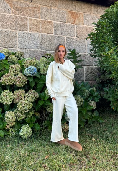 Sudadera color crema y pantalones acampanados a juego hechos de material suave. Presenta un corte holgado y una superficie texturizada. Complementado con zapatos marrones.