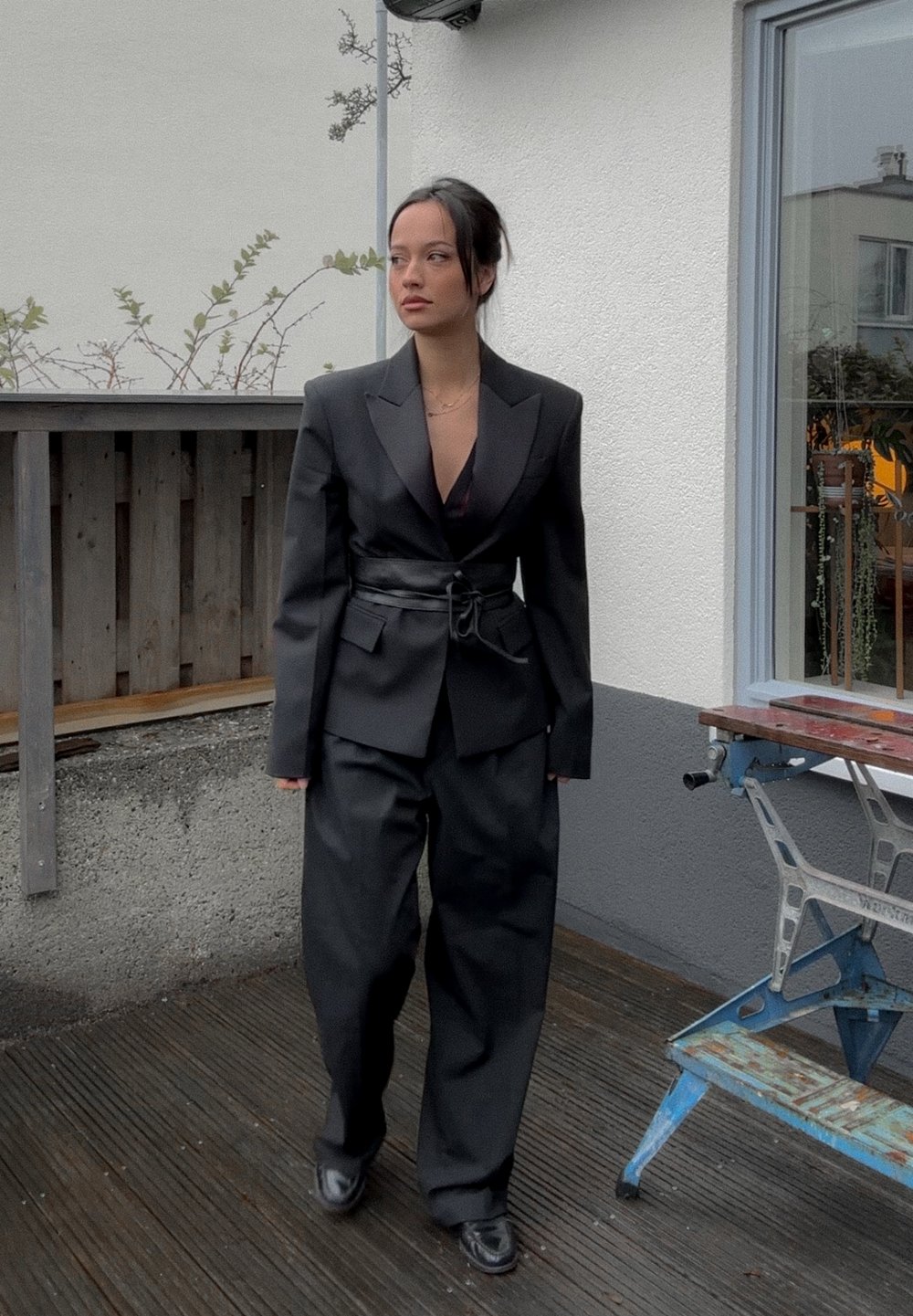 Traje negro a medida con blazer oversized y pantalones de pierna ancha. El blazer cuenta con un cinturón en la cintura. Textura suave y silueta moderna.