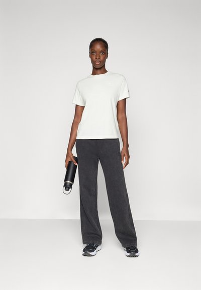 Camiseta de manga corta gris claro, de corte relajado, combinada con pantalones de pierna ancha gris oscuro. El modelo sostiene una botella de agua negra. Los zapatos tienen un diseño deportivo.