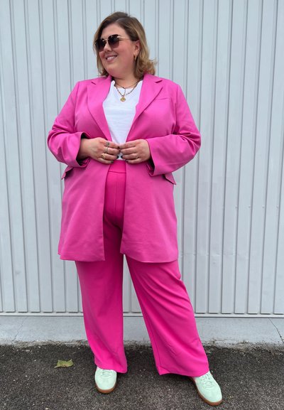 Blazer rosa de gran tamaño y pantalones a juego hechos de una tela suave, combinados con una camiseta blanca y zapatillas verde menta. Acentuado con joyería.
