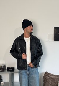 Mustast nahast jakk kahe esitaskuga, nööpkinni, kantud valge t-särgi peal. Sobitatud hele siniste teksade ja musta mütsiga.