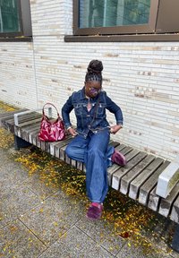 Denim jakna in široke hlače v temno modri barvi, puhasti maroon copati in sijoča rdeča torbica na leseni klopi, obdani z jesenskimi listi.