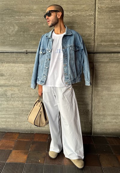 Chaqueta de mezclilla azul claro sobre una camiseta blanca, pantalones de pierna ancha a rayas y bolso beige. Gafas de sol negras completan el atuendo.
