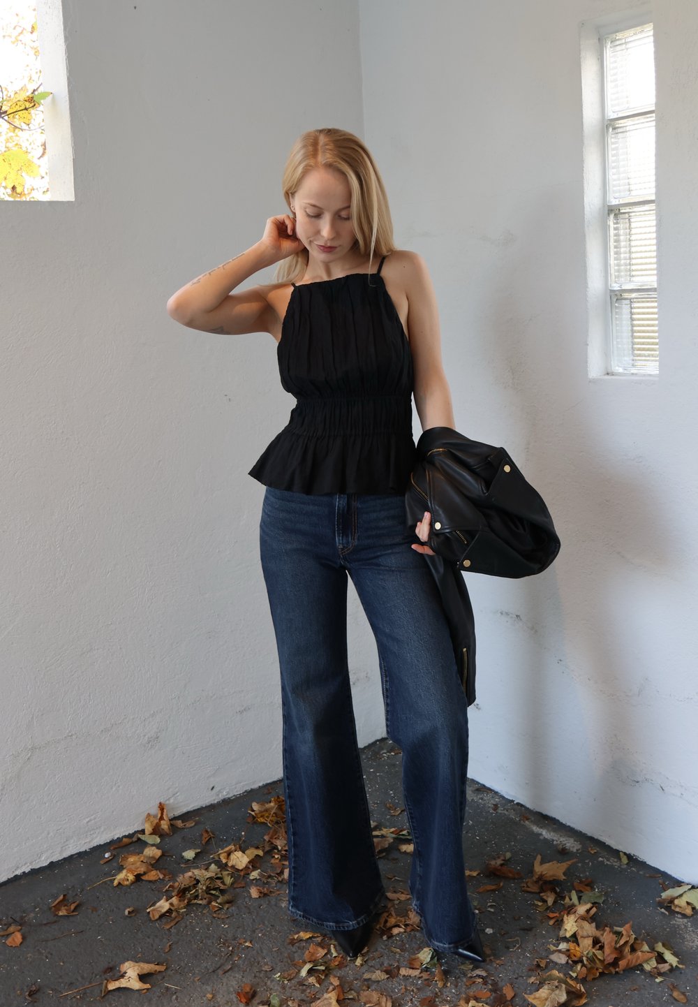 Zwarte, strapless peplumtop met opgehoopte textuur, gecombineerd met hooggetailleerde, wijde blauwe jeans. Zwarte leren jas over de arm gedragen.