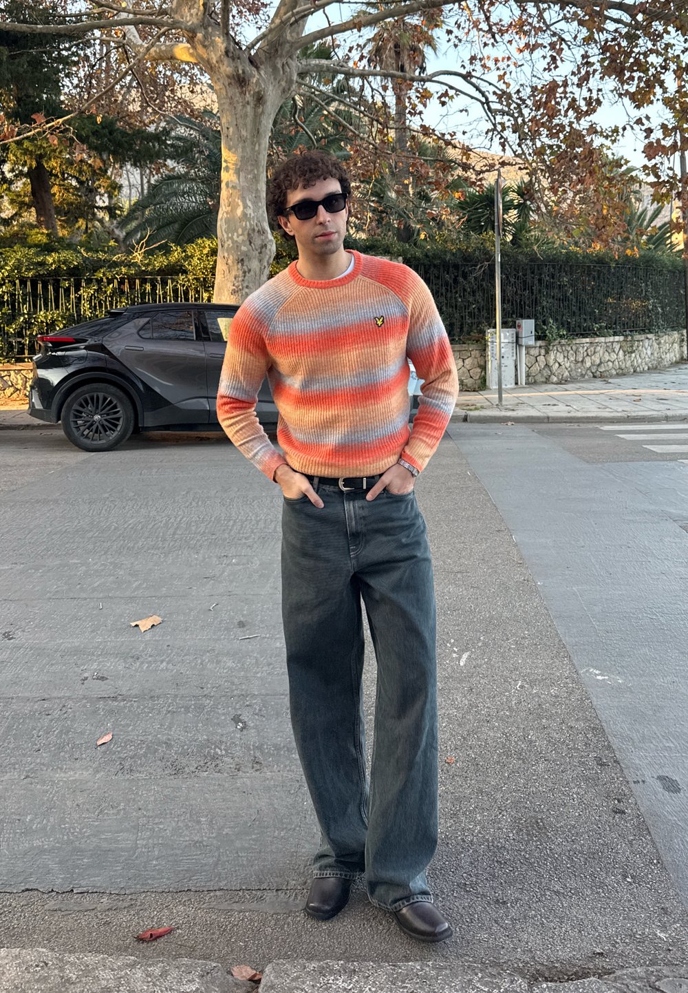 Pull multicolore avec des rayures allant de l'orange au bleu clair, tricot texturé, associé à un jean large foncé et des chaussures noires à enfiler.