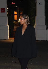 Svart oversized blazer med innsnevret midje, kombinert med svarte bukser. Bakgrunnen har dempet utendørsbelysning og grøntområde.