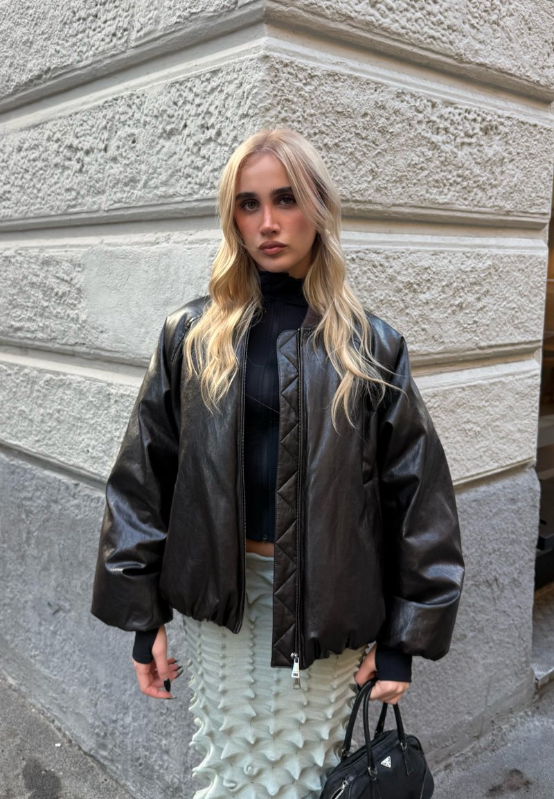 Svart läderbomberjacka med kviltad design, ribbade muddar och dragkedja; kombinerad med en texturerad ljus kjol.