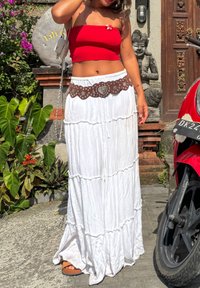 Witte gelaagde maxi-rok met een bruin decoratief riem met zilveren studs en een hartontwerp. Het topje is een rood geribbeld strapless crop-top.