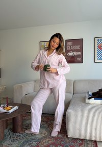 Różowo-biały piżamowy komplet w paski obejmuje koszulę zapinaną na guziki i pasujące spodnie. Tkanina wydaje się miękka, zapewniając swobodny krój.