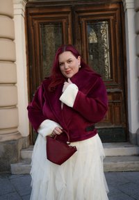 Bordó színű karosszéria velúr dzseki fehér köt�ött mandzsettákkal, réteges fehér tüll szoknyával és háromszög alakú, bordó színű hozzáillő kézitáskával párosítva.