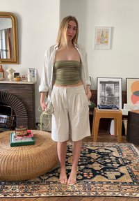 Light green strapless top worn with cream pleated shorts, a white button-up shirt, and beige flip-flops. Accessory: small shoulder bag.