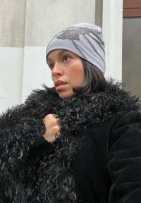 Bonnet en tricot gris avec un motif texturé, associé à un col en fausse fourrure noire et duveteuse. Mise au point sur les détails du tissu et les couleurs contrastées.