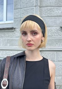 Μαύρο αμάνικο τοπ με δερμάτινο μπουφάν, κοντά ξανθά μαλλιά, μαύρη κορδέλα στο κεφάλι και ασημένια σκουλαρίκια κρίκοι σε φόντο με υφή γκρίζου χρώματος.