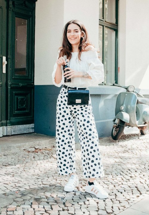 Csíkos rövidujjú felső, fekete szoknya és két tónusú hegyes sarkú cipő (fehér és fekete), amelyet egy víz mellett ülő személy visel.