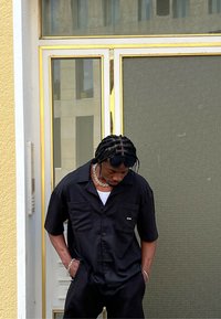 Musthave musta lühikeste varrukatega särk, millel on tekstureeritud muster, kaks esikotti ja väike logo, kombineerituna mustade tekstureeritud pükstega.