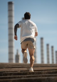 Sportieve man in een wit shirt en beige shorts, die op betonnen trappen omhoog rent met shorts met een klein blauw patroon.
