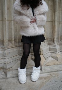 Umetno krzno kremno bele barve, črno nabrano mini krilo, neprosojne črne nogavice in beli puhasti snežni škornji z vezalkami. Gladke teksture.