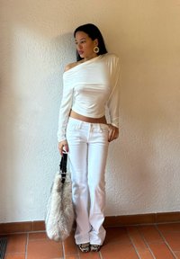 White long-sleeve top with off-shoulder design, paired with white flared pants. Accessories include a fuzzy handbag and patterned heels.