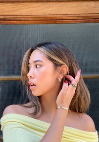 Modèle portant un haut jaune décolleté, des boucles d'oreilles en argent et plusieurs anneaux, avec de longs cheveux texturés et une coiffure ajustée.