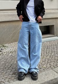 Világoskék, bőszárú farmernadrág, magas derékkal és kopott hatású textúrával. Fekete platform cipővel és fekete dzsekivel kombinálva.