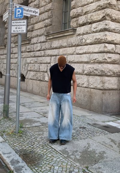 Top negro sin mangas con escote en V; pantalones vaqueros de mezclilla azul claro de corte holgado con una textura desgastada; de pie en una calle de adoquines.