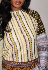 Pull en tricot multicolore à rayures verticales jaunes, brunes et blanches ; présente des motifs complexes et des textures variées sur les manches.