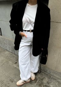 Blazer noir sur un t-shirt blanc col rond, ceinturé avec une boucle dorée ; pantalon blanc ample et baskets légères avec un design texturé. Sac noir.