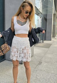 Λευκή πλεκτή φούστα με λουλουδάτο μοτίβο, λευκό κοντομάνικο τοπ, μαύρο τζάκετ και τσάντα λεοπάρ. Γυαλιά ηλίου και κοσμήματα με πέρλες ως αξεσουάρ.