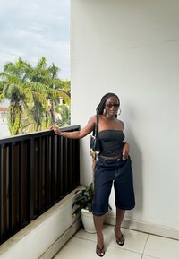 Top nero senza spalline, culotte in denim scuro e sandali neri. Gli accessori includono grandi orecchini a cerchio in oro e una piccola borsa nera.