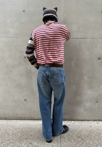 Pasiasta czerwona i biała koszulka, rękawy w wzory, w połączeniu z niebieskimi dżinsami i czarnym obuwiem; na głowie dziergana czapka z uszami.
