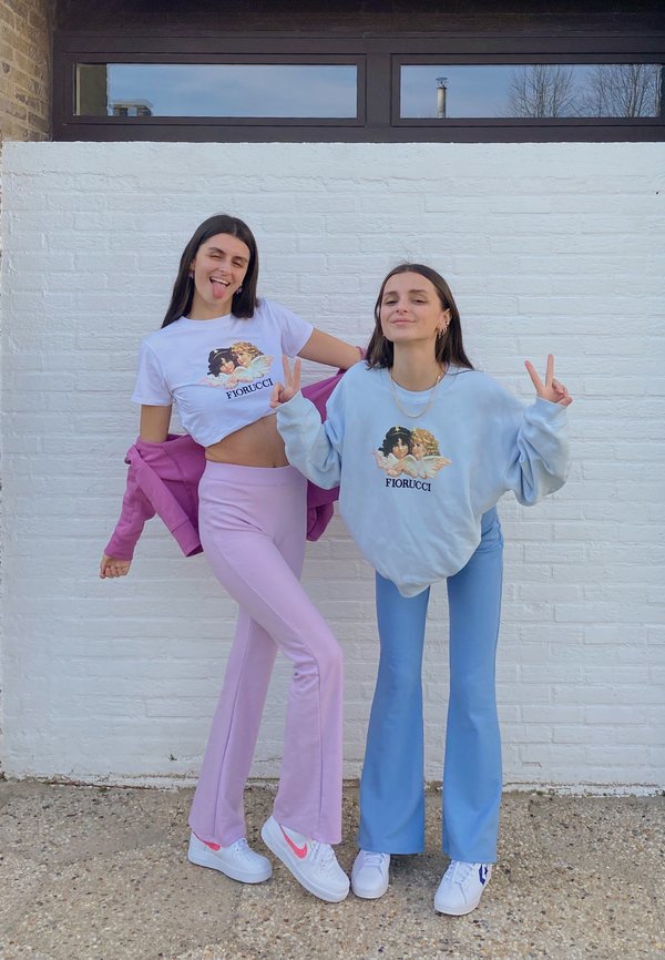 Dos modelos lucen camisetas gráficas y pantalones de campana. Una camiseta es blanca con un estampado colorido, mientras que la otra es de color azul claro. Los pantalones son de tonos pastel.