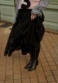 Svart skjørt med volanger i teksturert stoff, kombinert med skinnende svarte snøresko med spisse tær og ankelhøye hæler.