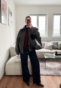 Giacca di pelle nera con colletto alto, top bordeaux, jeans neri a gamba larga e stivali neri a punta. Borsa nera spaziosa e decorazioni minime.