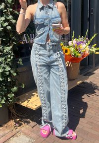 Denim halter top with a cropped design and wide-leg jeans featuring side lacing details. Bright pink platform sandals complete the look.