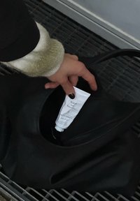 Sac à main en cuir noir à la texture lisse, avec une grande ouverture. Un tube blanc de crème pour les mains est partiellement visible à l'intérieur.