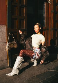 Veste surdimensionnée en cuir marron, crop top jaune à motifs, leggings en dentelle rouge et bottes montantes blanches à motifs ; petit sac à main à motifs.