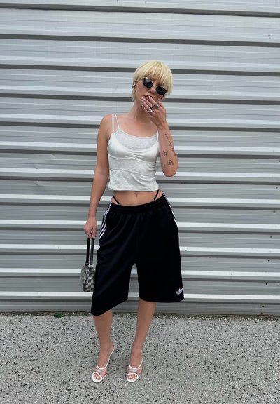 Top ajustado blanco, pantalones cortos deportivos negros con rayas blancas, sandalias de tacón cuadrado transparente y bolsa de mano pequeña con un patrón.