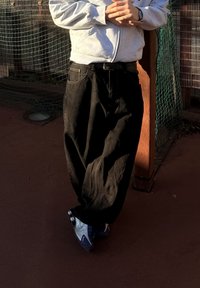 Schwarze, lässige Hosen mit strukturiertem Finish, getragen mit einem grauen Reißverschluss-Hoodie. Blaue Sportschuhe mit einer weißen und schwarzen Sohle.