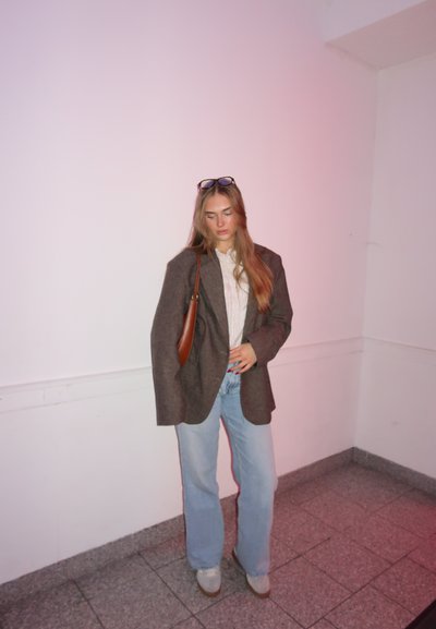Blazer marrón oversize, camisa blanca con cuello, vaqueros de pierna ancha azul claro y zapatos de plataforma grises; bolso de hombro marrón; entorno minimalista.