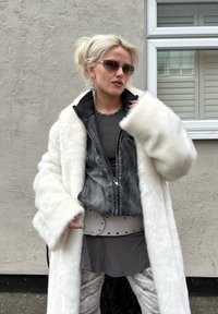 Bílý kabát z umělé kožešiny, šedá džínová bunda s �žebrovaným límcem, šedé tílko, světle šedý pásek s cvočky a kalhoty s potiskem.