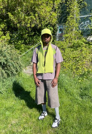 Gorra verde y bufanda, camiseta gris de gran tamaño con acentos verdes, culottes grises, calcetas grises y zapatillas deportivas blancas, en un entorno verde.