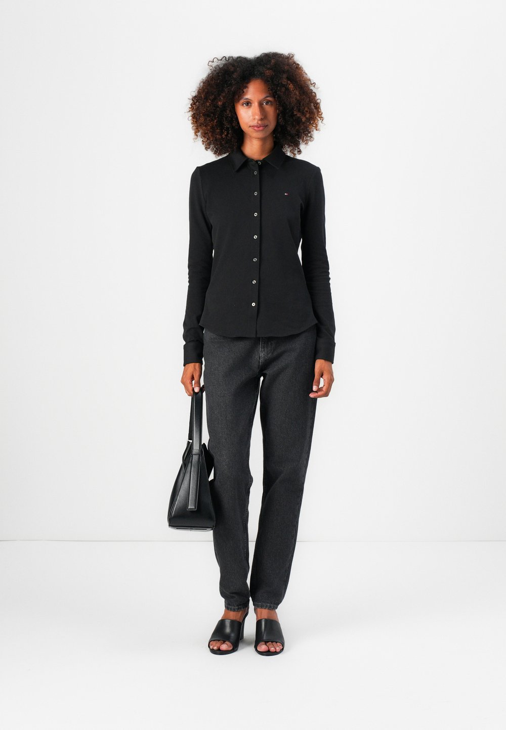 Black long-sleeved button-up shirt with a collar, teamed with dark grey jeans, black slide sandals, and a black handbag. Simple design.